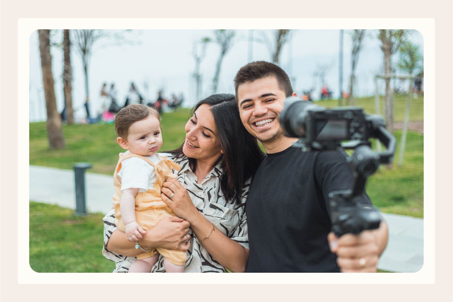 Family of woman holding baby and man with arm around them holding camera for selfie video