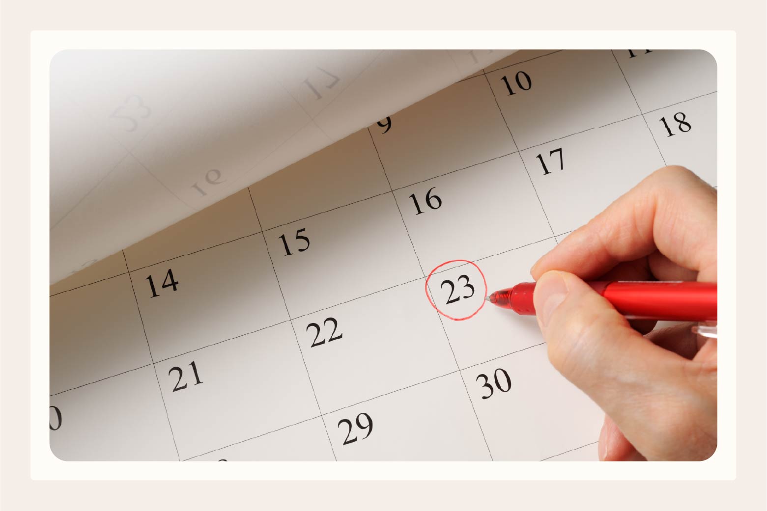Close up of a hand with red pen circling the 23rd on a monthly calendar