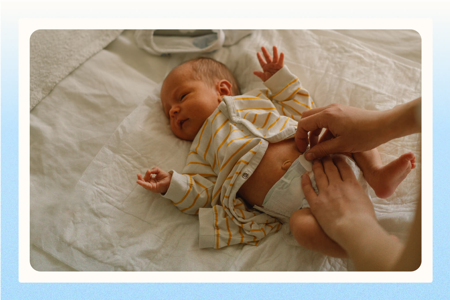 Parents hands closing tab of disposable diaper onto infant laying on white fabric surface