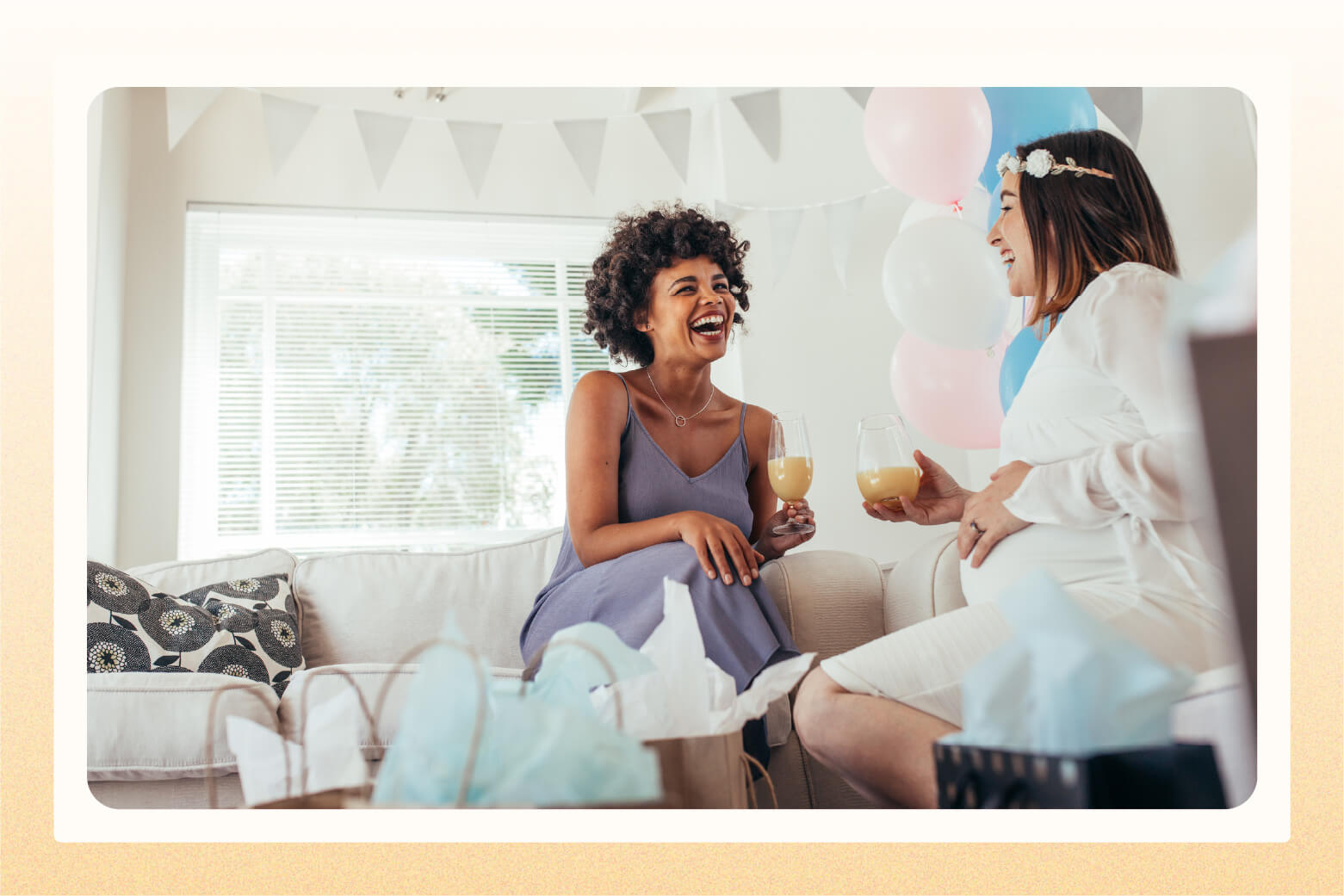 Two laughing women, one who's pregnant, sit in living room decorated for baby shower 