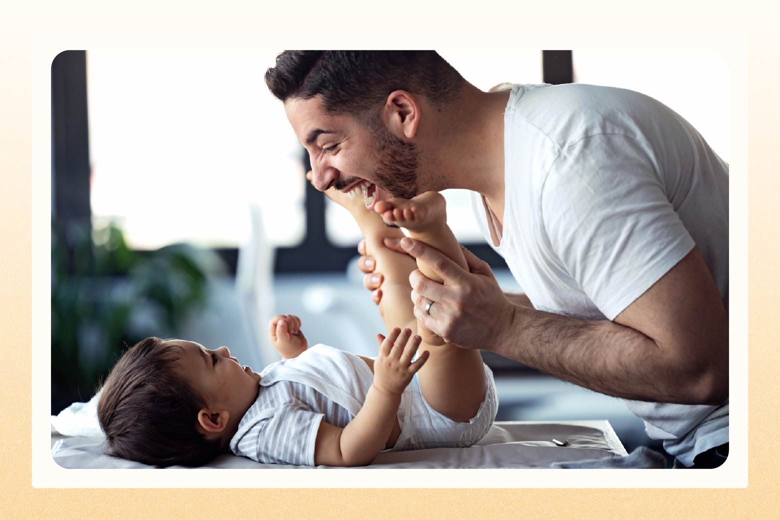 Man laughing while playing with the legs and feet of a happy baby