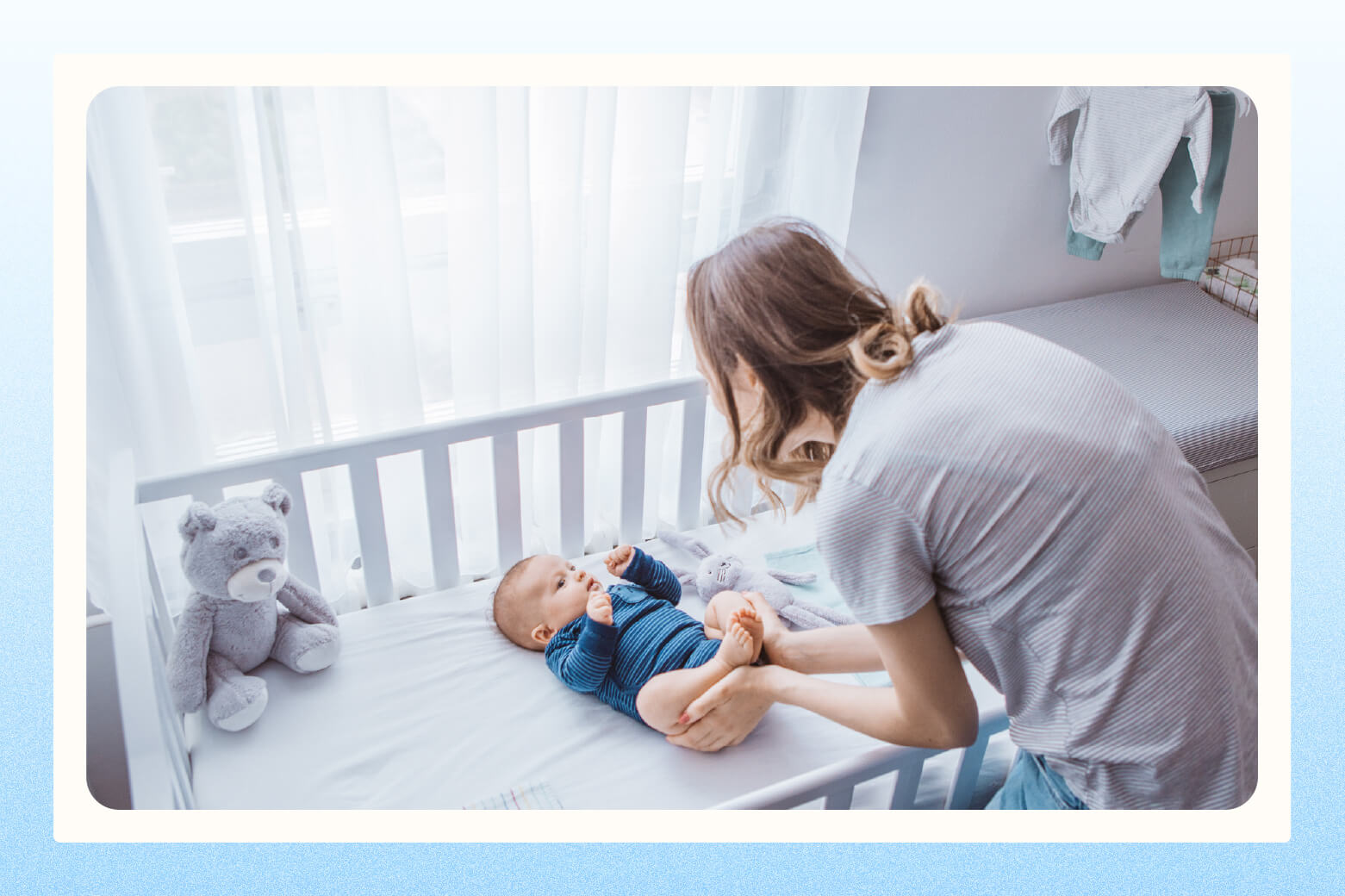 Woman leaning over dropped edge of a convertible crib to play with baby
