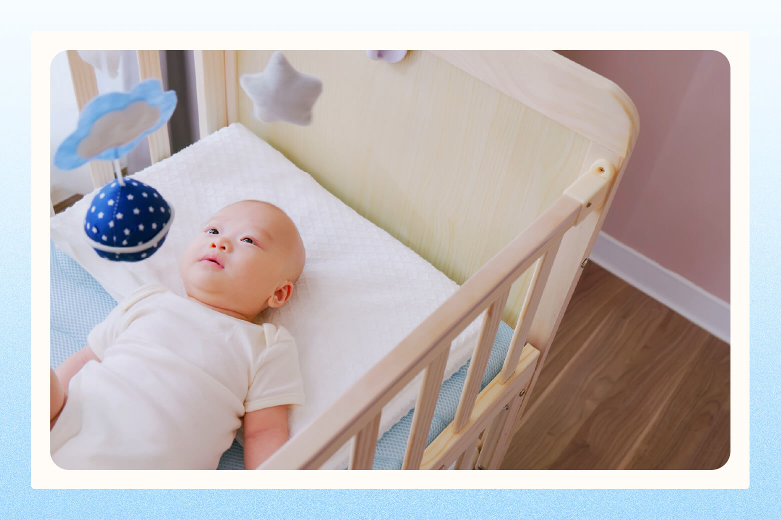Overhead close-up view of baby laying in small mini crib staring at mobile 