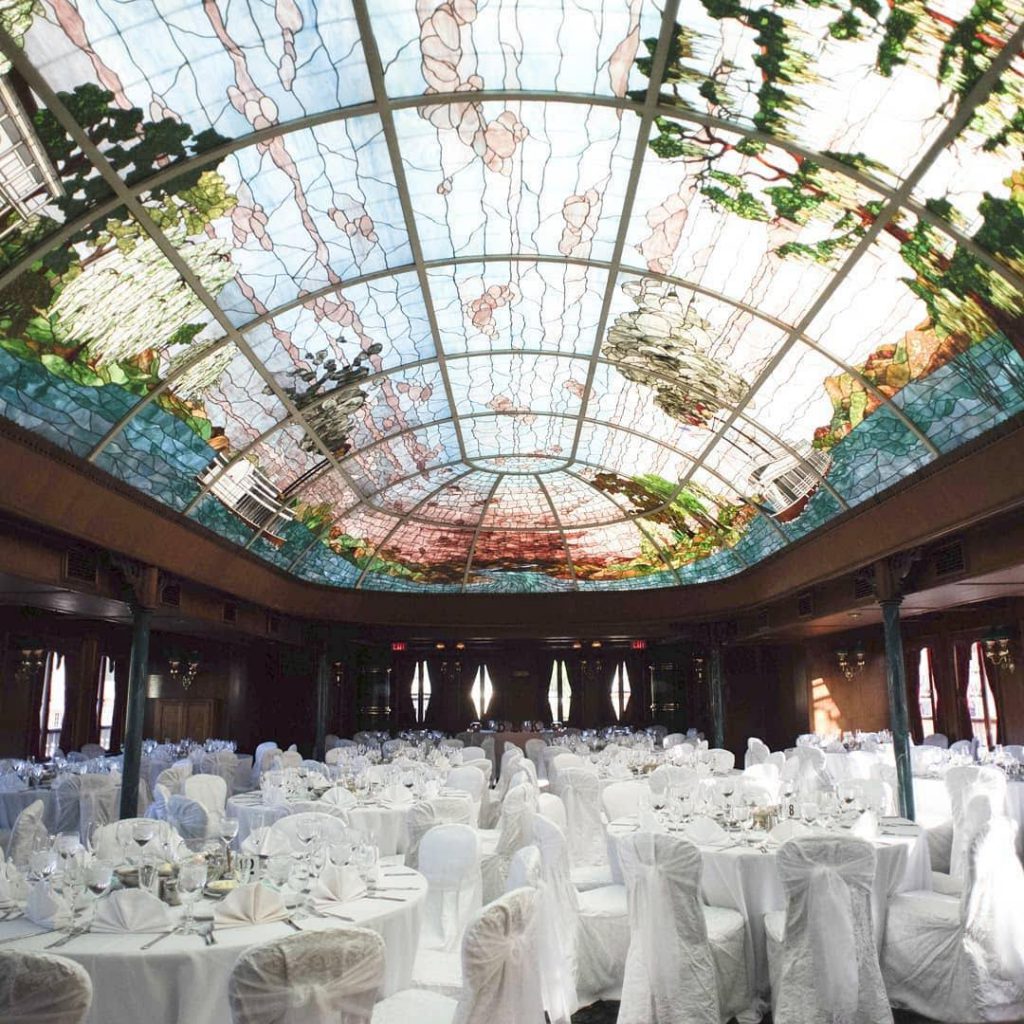 reception setup with white chairs and tables under stained glass ceiling at bahia resort hotel in san diego