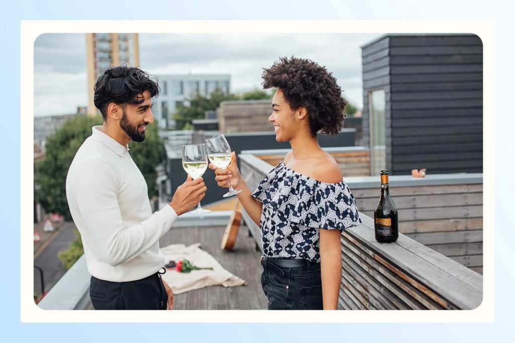 A couple clinking wine glasses having a picnic on a rooftop